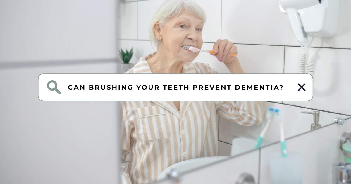 Elderly woman brushing her teeth in the bathroom while smiling at the mirror, illustrating the connection between mouth and dementia prevention.