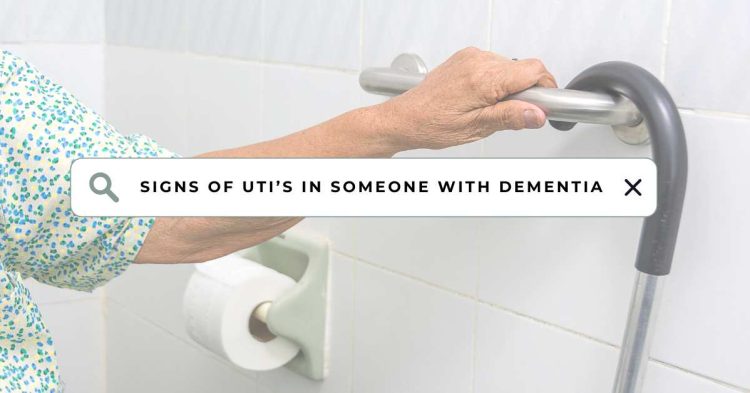 An elderly person with dementia gripping a bathroom grab bar for support, with a walker nearby. A search bar overlay reads ‘Signs of UTI’s in Someone with Dementia,’ highlighting the focus on UTI awareness and prevention in dementia patients.